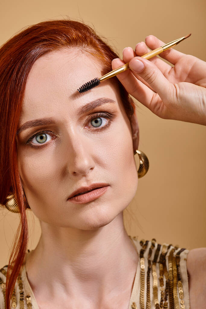 portré vörös hajú nő zöld szemekkel alkalmazó szempillaspirál bézs háttér, smink - Fotó, kép