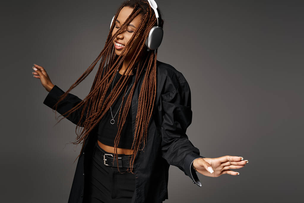 alegre y joven mujer afroamericana de 20 años con auriculares bailando con música sobre fondo gris - Foto, Imagen