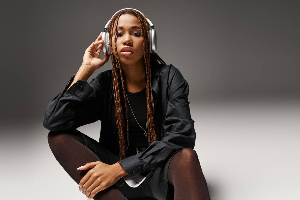молода афроамериканка 20-х років з дредлоками насолоджується музикою в стильних навушниках на сірому - Фото, зображення