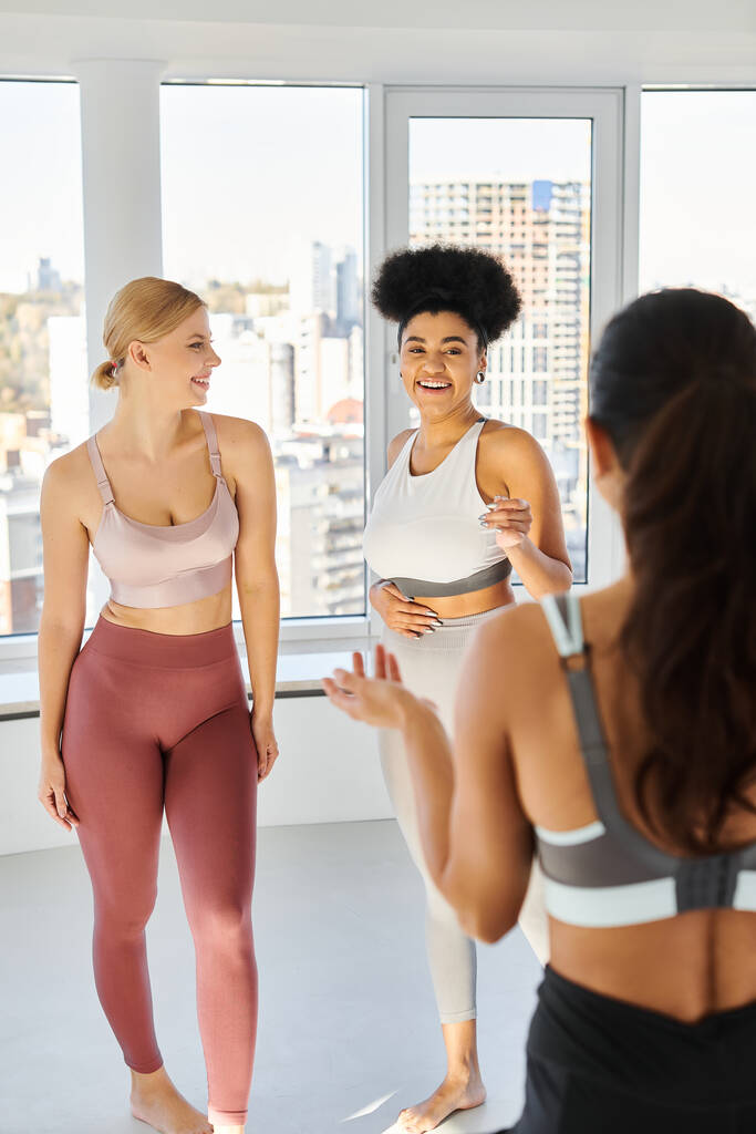 female pilates trainer talking to happy multiethnic woman in sportswear before class, sport - Photo, Image