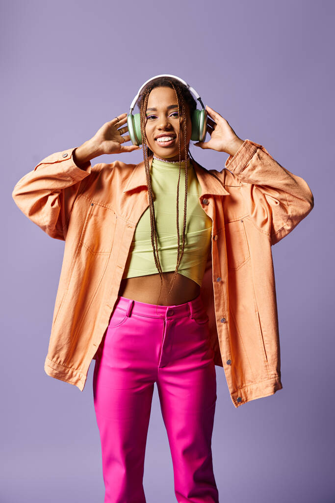 ワイヤレスヘッドフォンで幸せなアフリカ系アメリカ人の少女と紫色の背景に活気に満ちたカジュアルな服装 - 写真・画像