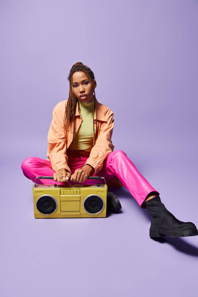 elegante mujer afroamericana con rastas sentado junto a boombox retro sobre fondo púrpura - Foto, imagen