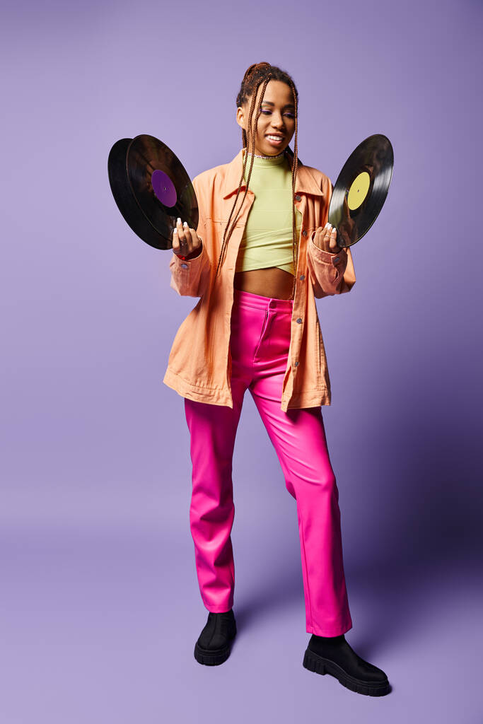 šťastný africký americký dívka ve svých 20s s dredy srovnávání vinyl disky na fialové pozadí - Fotografie, Obrázek