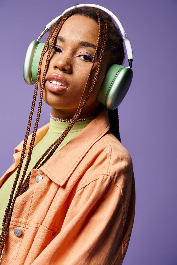 jolie fille afro-américaine dans les années 20 écouter de la musique dans des écouteurs sans fil sur fond violet - Photo, image