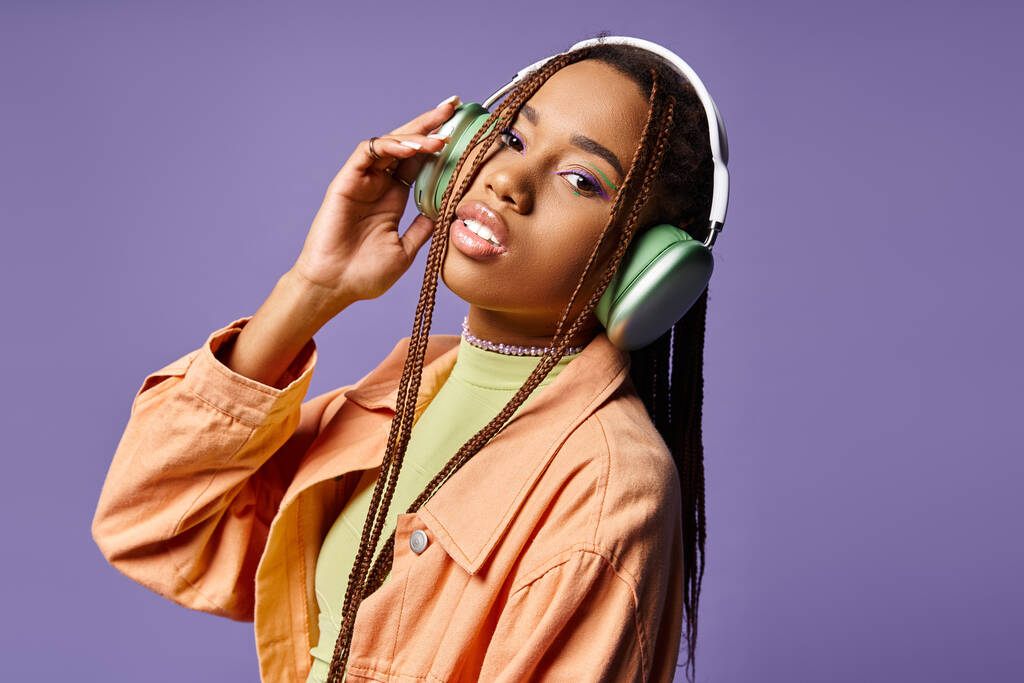 όμορφη Αφροαμερικανή γυναίκα στα 20 ακούει μουσική σε ασύρματα ακουστικά σε μωβ φόντο - Φωτογραφία, εικόνα