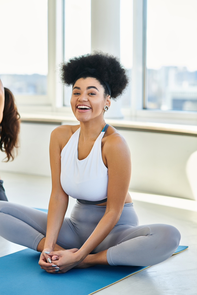 veselé Afroameričanky ve sportovním oblečení sedí na podložce a těší jóga třídy uvnitř - Fotografie, Obrázek