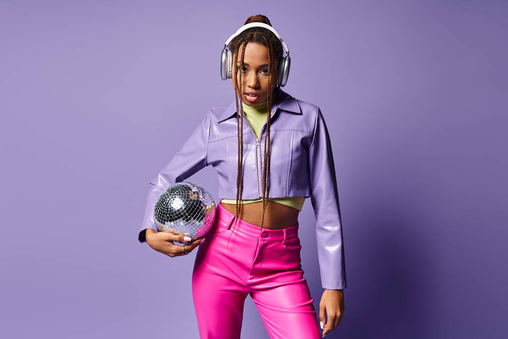 fiatal afro-amerikai nő divatos öltözékben és fejhallgató kezében disco labda lila háttér - Fotó, kép