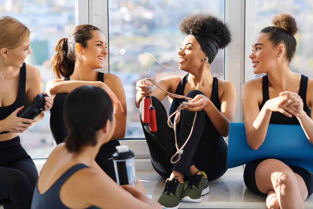 group of happy and young interracial women in active wear chatting after workout in pilates studio - Photo, Image