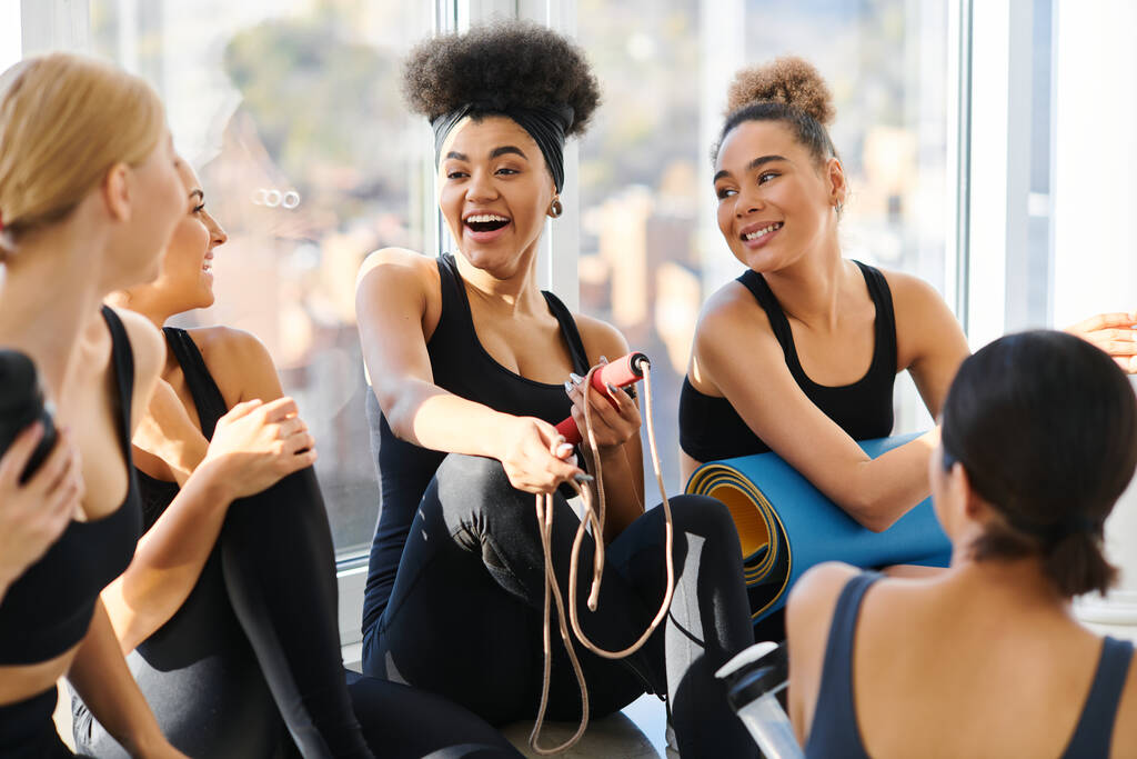 Gruppe fröhlicher junger interrassischer Frauen in aktiver Kleidung plaudert nach dem Training im Pilates-Studio - Foto, Bild
