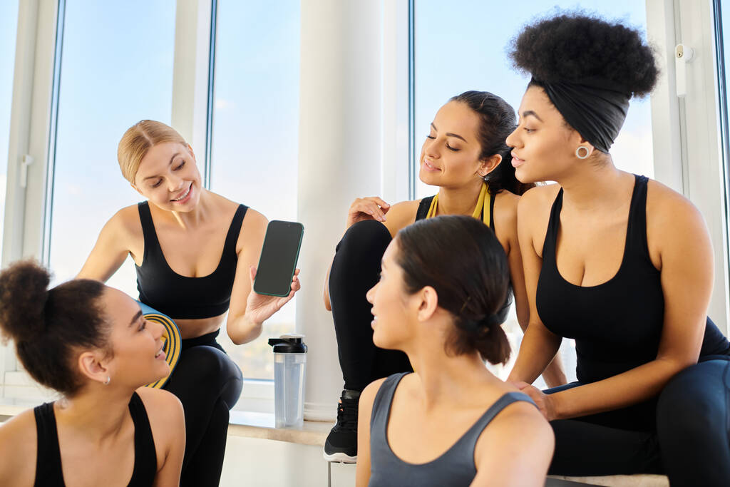 молода блондинка показує смартфон своїм друзям після тренування в студії йоги - Фото, зображення