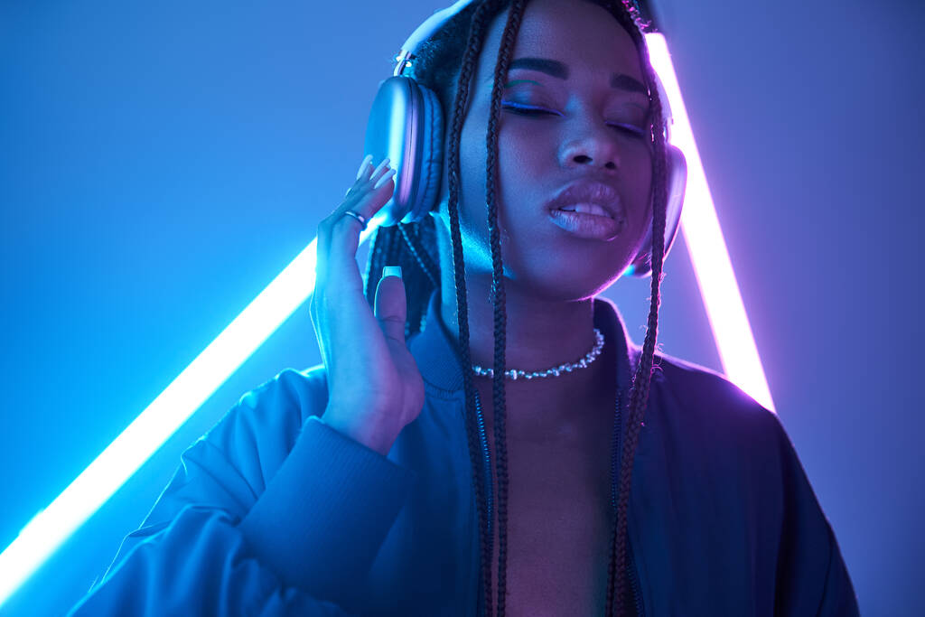 чарівна афроамериканська жінка в навушниках насолоджується музикою в студії з люмінесцентним світлом - Фото, зображення