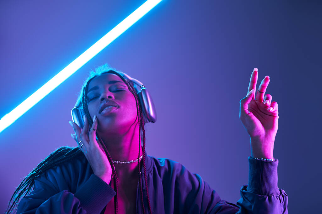 ヘッドフォンのエクスタシーなアフリカ系アメリカ人女性は蛍光灯でスタジオで音楽を楽しんでいます - 写真・画像