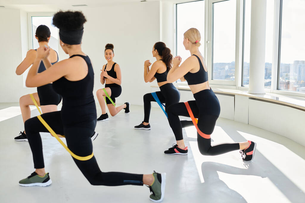 group of diverse women in sportswear looking at happy trainer and doing lunges with resistance bands - Photo, Image