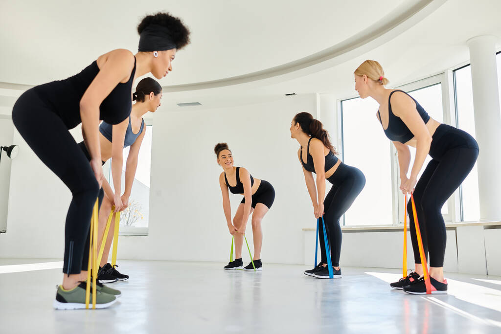 young diverse women looking at happy pilates instructor and working out with resistance bands - Photo, Image
