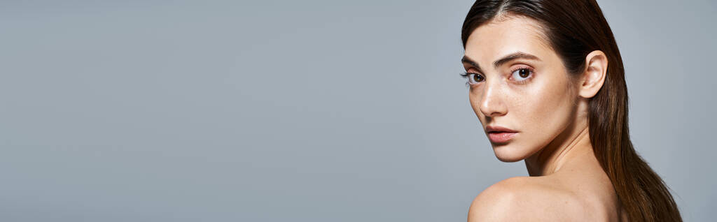Uma jovem mulher caucasiana com cabelos castanhos longos fica sem camisa, exalando uma sensação de liberdade e beleza em um estúdio, banner - Foto, Imagem