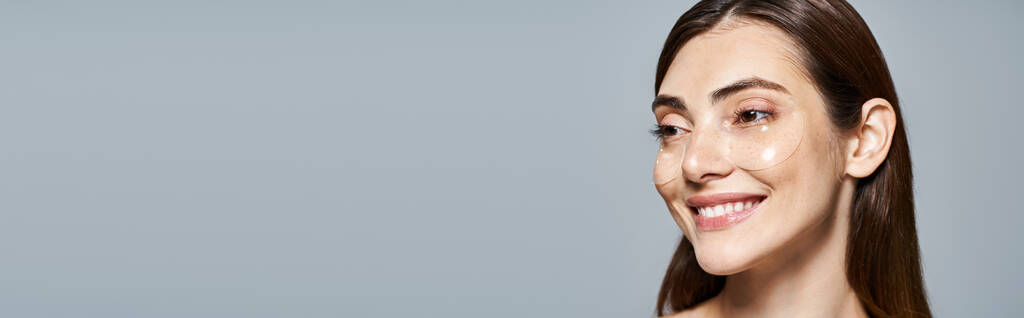 Młoda kaukaska kobieta z długimi brązowymi włosami uśmiecha się jasno do kamery w studio, pod opaską na oku - Zdjęcie, obraz
