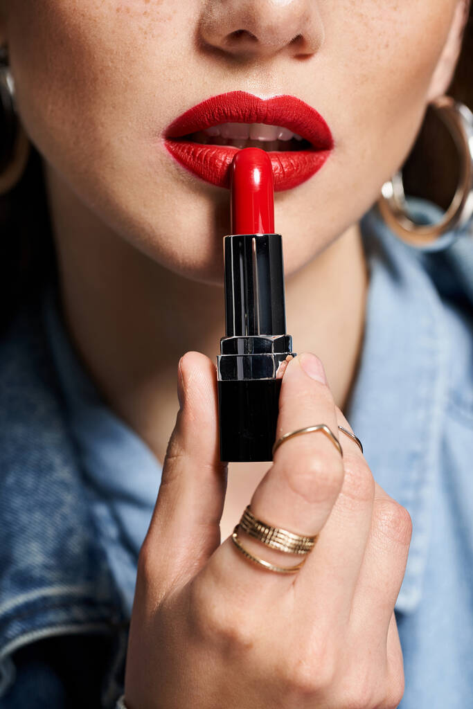 Una joven mujer sostiene un vibrante lápiz labial rojo en su mano, preparado para realzar su belleza. - Foto, imagen