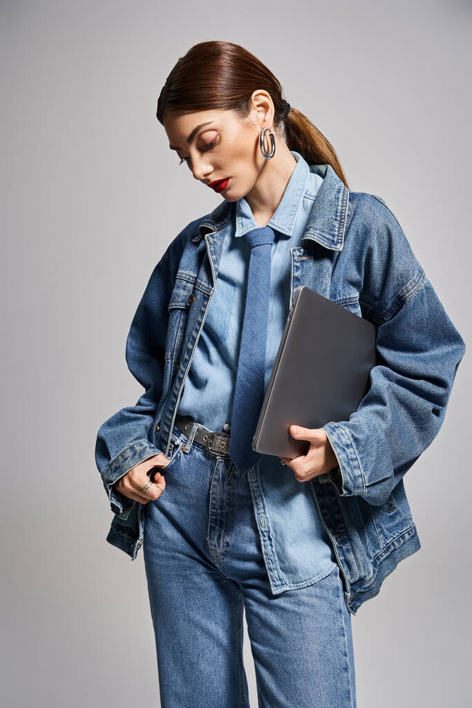 Молода кавказька жінка з брюнеткою волосся в джинсовій куртці тримає ноутбук, стоячи впевнено. - Фото, зображення