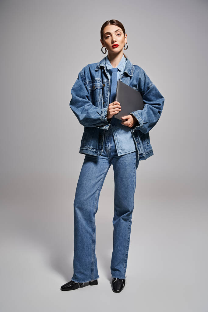 A young Caucasian woman with brunette hair confidently wearing a denim jacket and jeans, holding laptop - Photo, Image