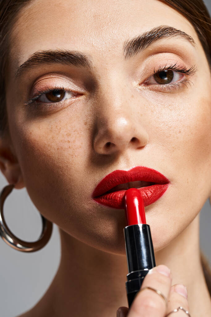 Una joven mujer caucásica con el pelo moreno usando lápiz labial rojo en los labios, exudando confianza y belleza. - Foto, imagen