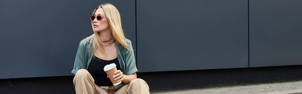 Eine Frau sitzt auf dem Boden und genießt eine Tasse Kaffee in einem ruhigen Moment im Freien. - Foto, Bild