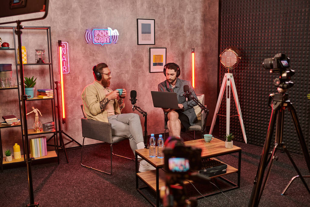 beaux hommes barbus avec écouteurs boire du café et parler activement pendant podcast - Photo, image