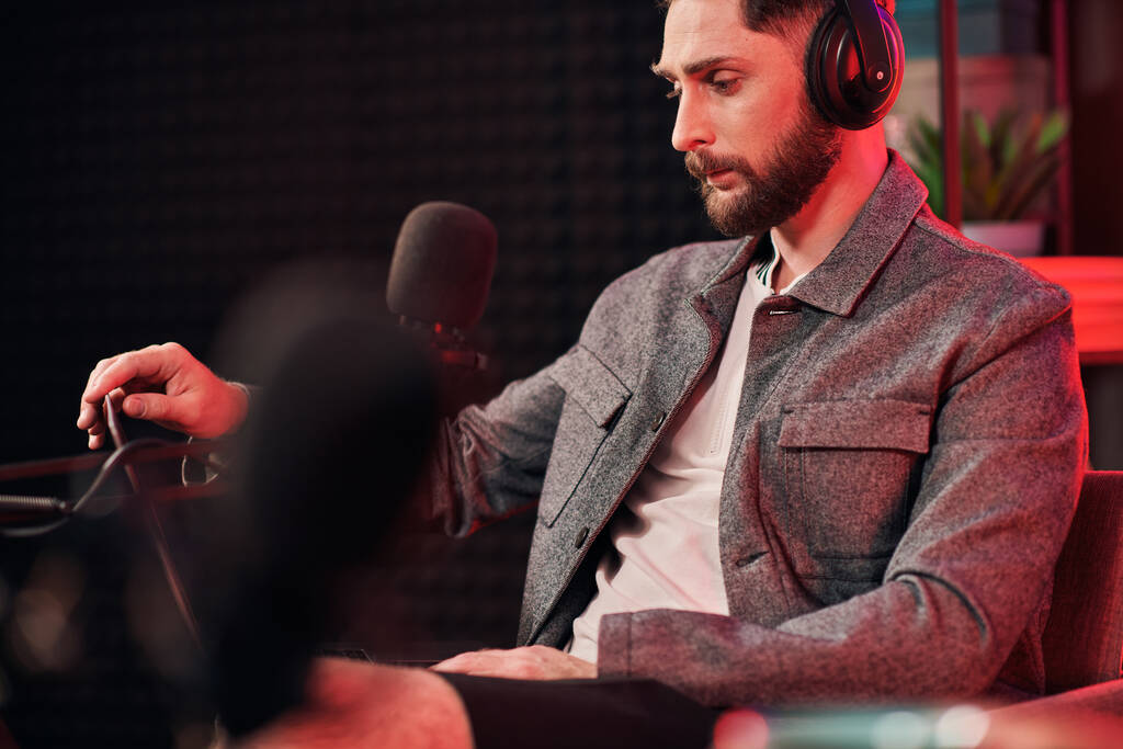Kulaklık takmış yakışıklı sakallı adam podcast sırasında stüdyoda oturuyor. - Fotoğraf, Görsel