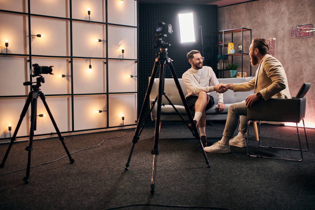 knappe elegante mannen met baarden in chique kleding schudden hun handen tijdens interview in de studio - Foto, afbeelding