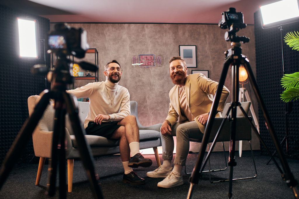 красивые радостные мужчины в элегантных нарядах, счастливо улыбающиеся в камеру во время интервью в студии - Фото, изображение