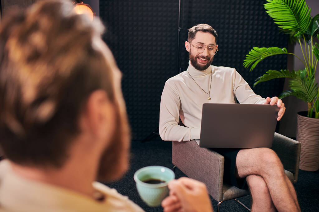 beaux hommes joyeux en tenues élégantes avec café et ordinateur portable discuter des questions d'entrevue - Photo, image