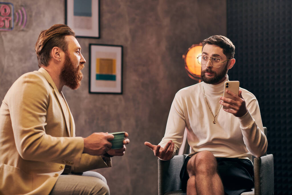 dos hombres elegantes guapos con barbas en ropa elegante mirando el teléfono inteligente durante la entrevista - Foto, Imagen