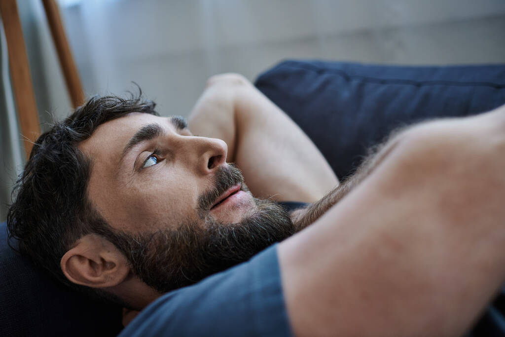 depressed bearded man in casual attire lying on sofa during breakdown, mental health awareness - Photo, Image