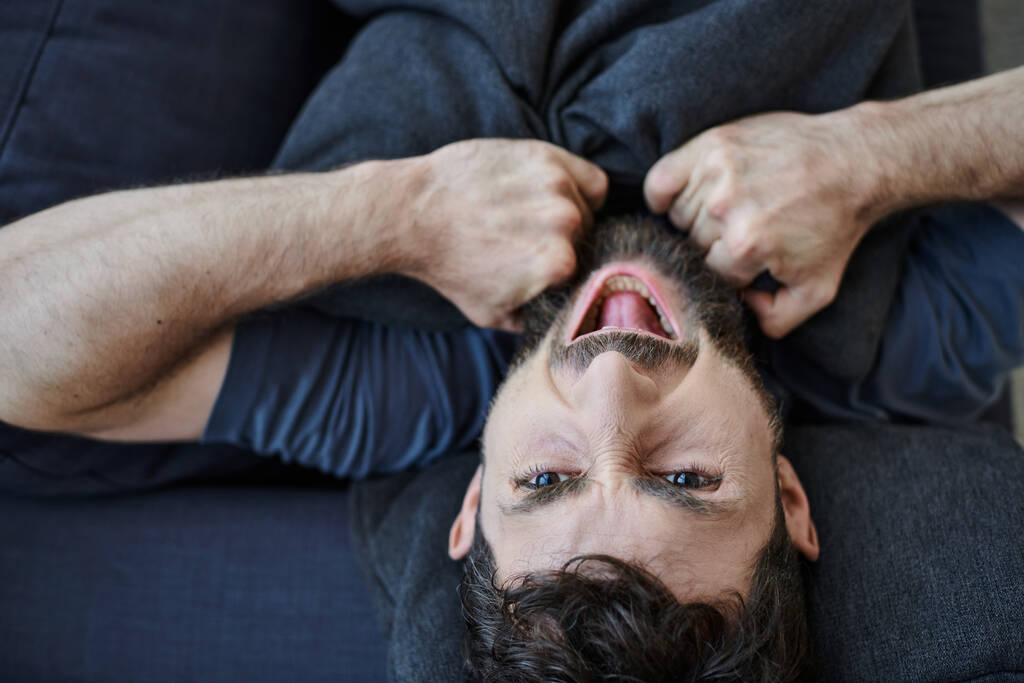barbuto depresso uomo in abiti casual urlando mentre sdraiato sul divano durante il crollo mentale - Foto, immagini