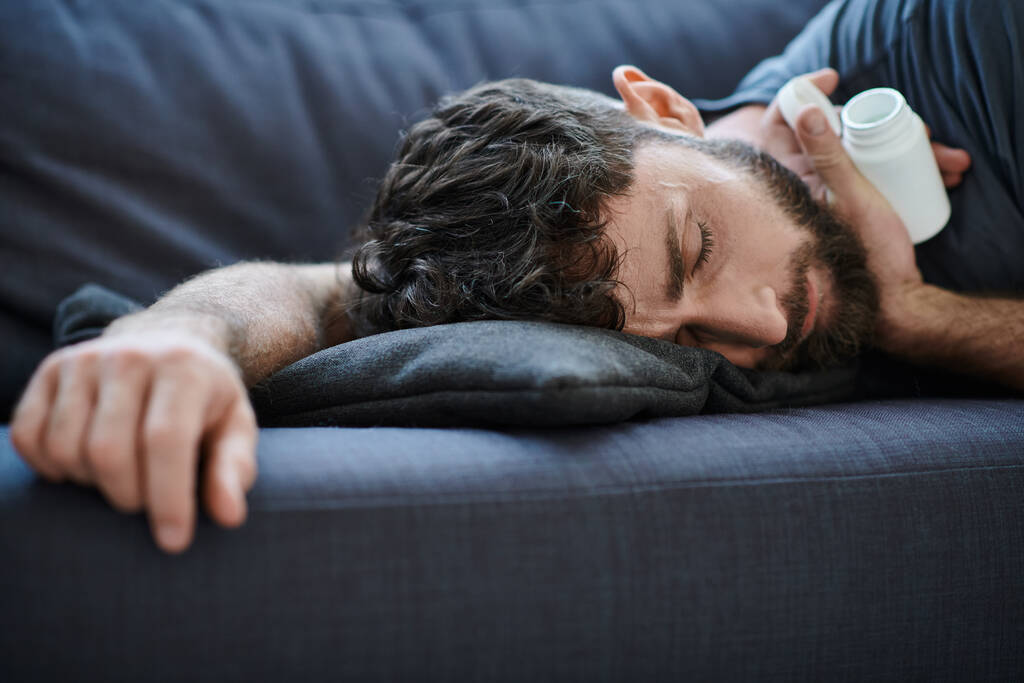 traumatisoitunut kärsimystä mies parta makaa sohvalla pillereitä kädessä, mielenterveyden tietoisuus - Valokuva, kuva