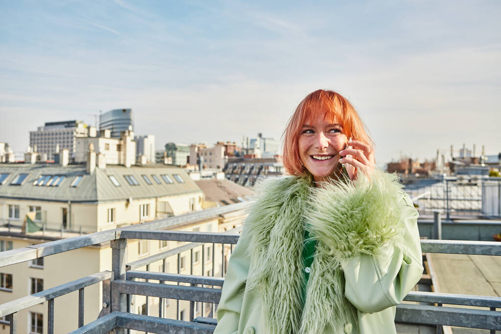 Eine lächelnde, stylische Frau, die auf dem Smartphone spricht und auf der Dachterrasse in Wien wegschaut - Foto, Bild