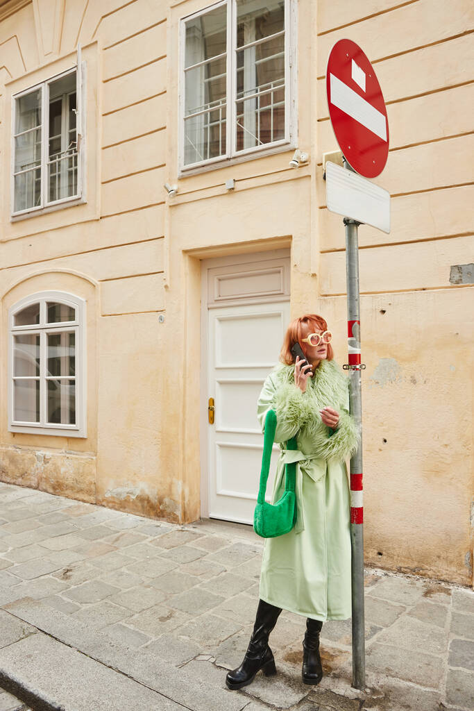 модная женщина в солнечных очках и в повседневной одежде разговаривает по смартфону на городской улице в Вене - Фото, изображение