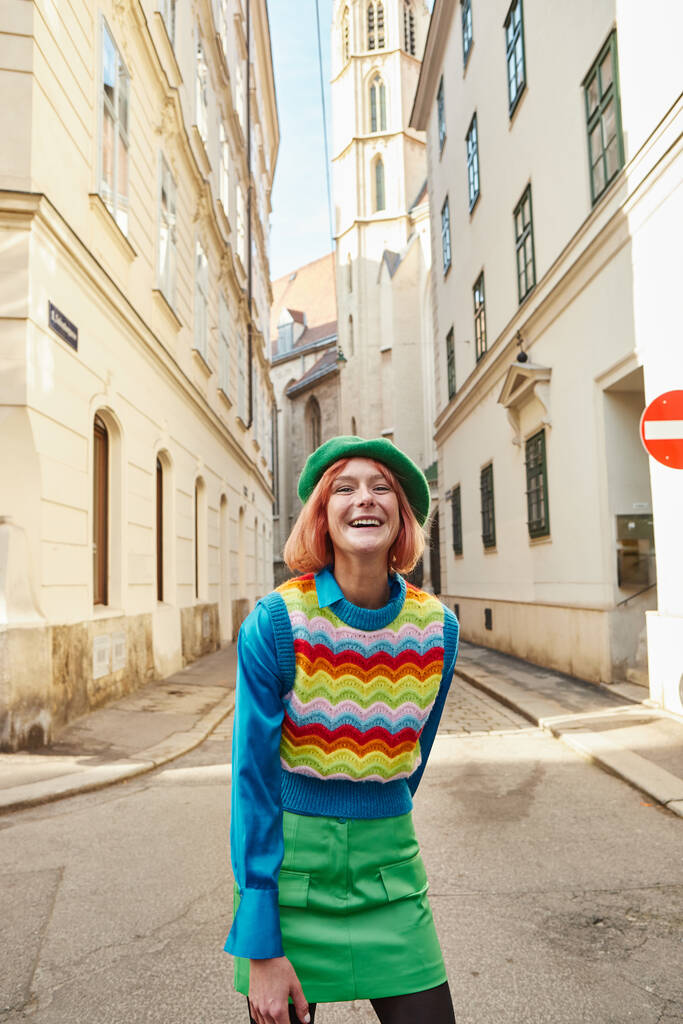 túlfűtött nő svájcisapkában és divatos ruhák nevetnek a kamera előtt Bécs utcáján, Ausztriában - Fotó, kép
