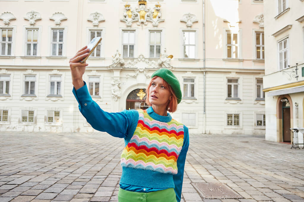 mujer de moda en chaleco colorido y boina tomando selfie en el teléfono inteligente en la calle en Viena - Foto, imagen