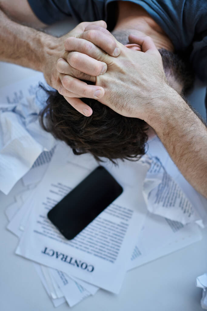 Top widok człowieka w depresji ze smartfonem z papierami i umowy w pobliżu niego podczas załamania psychicznego - Zdjęcie, obraz