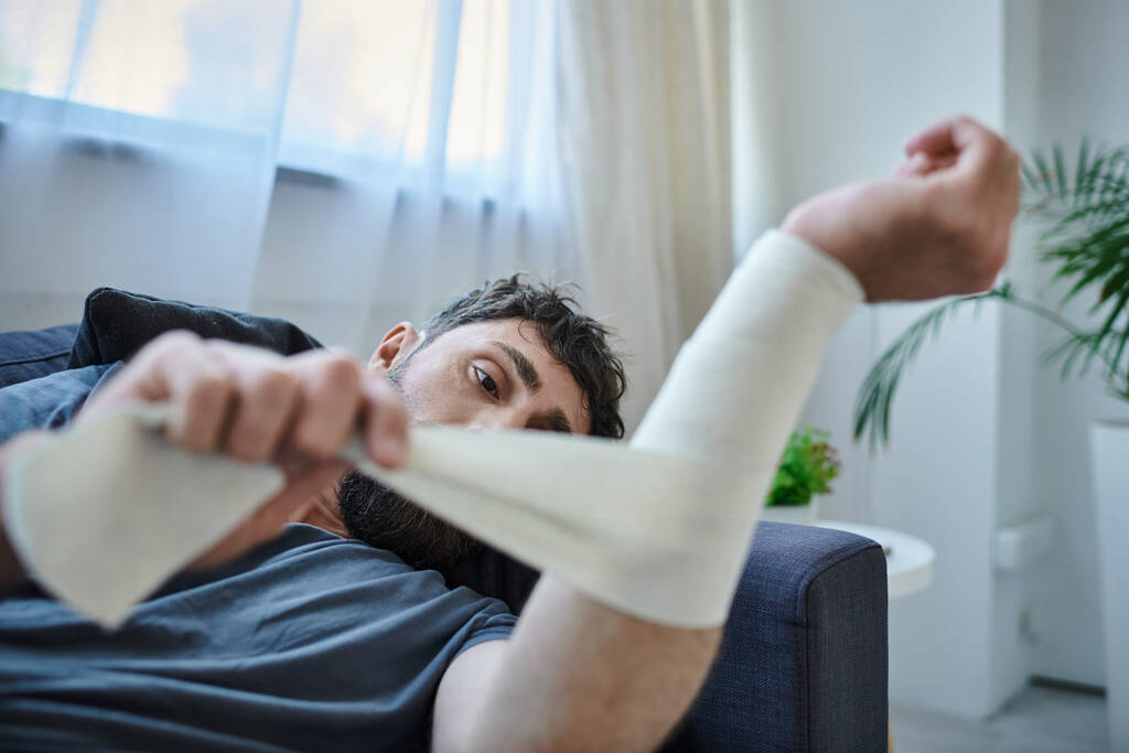 τραυματισμένος άντρας με επίδεσμο στο χέρι μετά από απόπειρα αυτοκτονίας ξαπλωμένος στον καναπέ, συνειδητοποίηση ψυχικής υγείας - Φωτογραφία, εικόνα