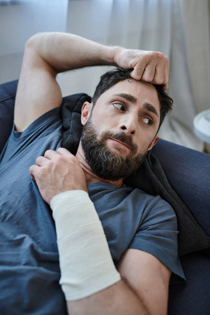 απελπισμένος άντρας με επίδεσμο στο χέρι μετά από απόπειρα αυτοκτονίας ξαπλωμένος στον καναπέ, συνειδητοποίηση ψυχικής υγείας - Φωτογραφία, εικόνα