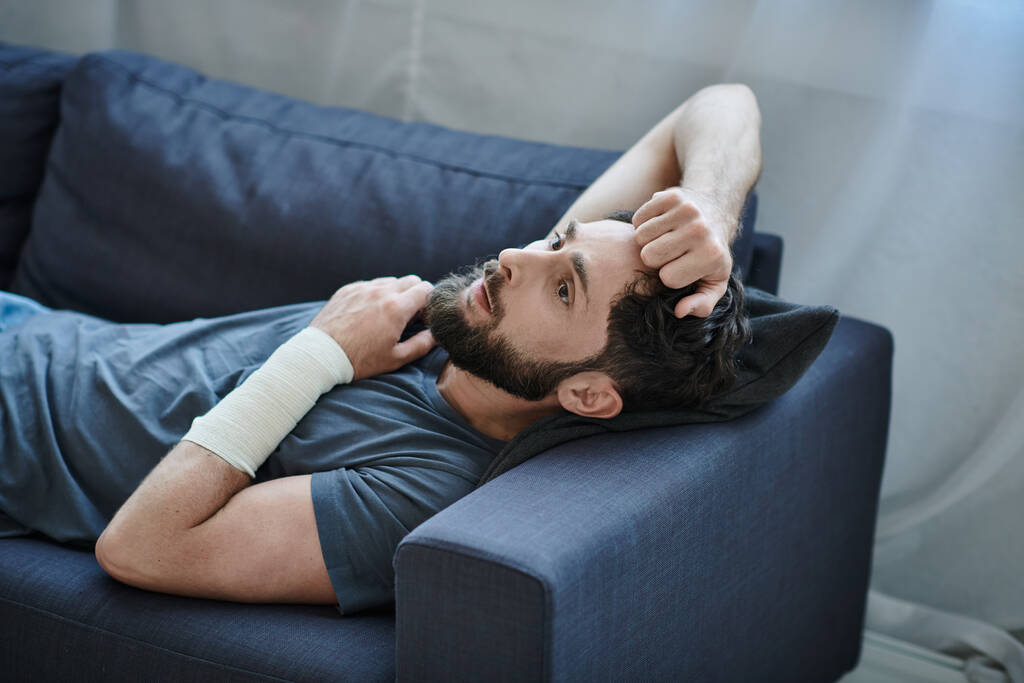 Verzweifelter Mann mit Verband am Arm nach Selbstmordversuch auf Sofa liegend, Bewusstsein für psychische Gesundheit - Foto, Bild
