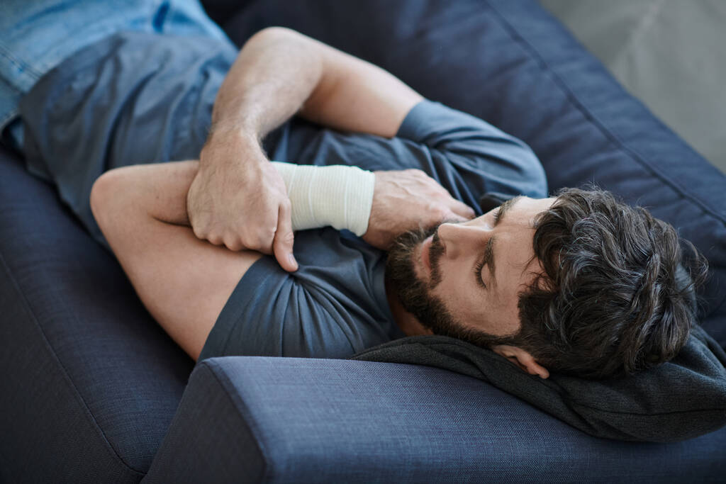 desperate man with bandage on arm after attempting suicide lying on sofa, mental health awareness - Photo, Image