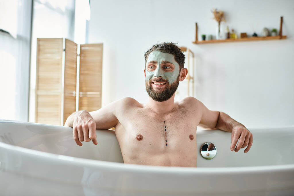 Χαρούμενος όμορφος άντρας με γενειάδα και μάσκα προσώπου να παγώνει στην μπανιέρα του, συνειδητοποίηση ψυχικής υγείας - Φωτογραφία, εικόνα