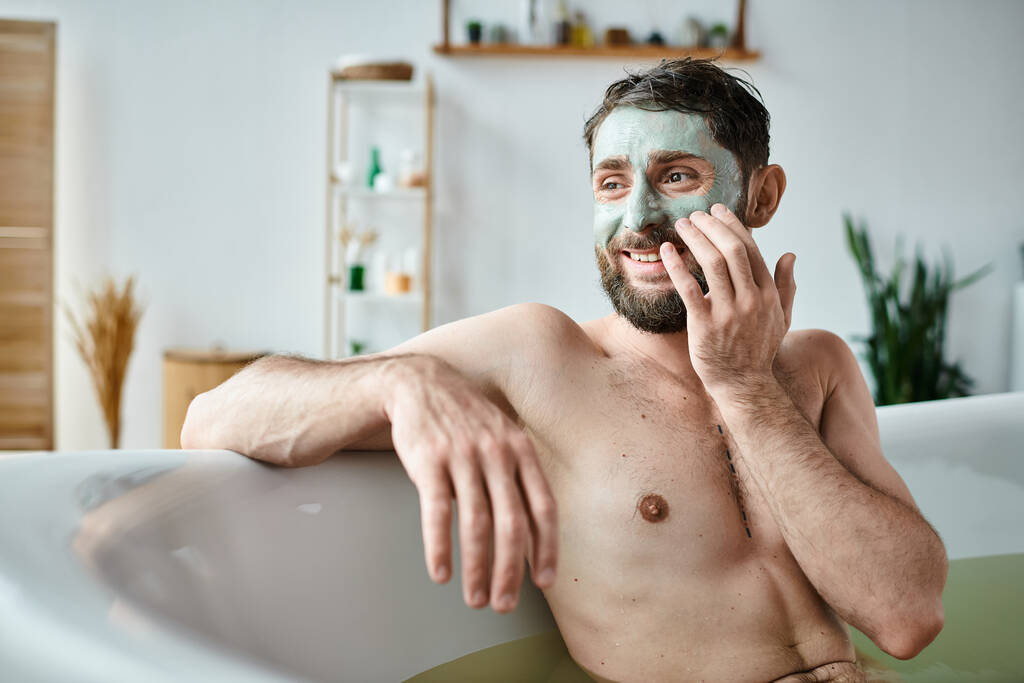 iloinen komea mies, jolla on parta ja kasvonaamio jäähdytys kylpyammeessa, mielenterveystietoisuus - Valokuva, kuva
