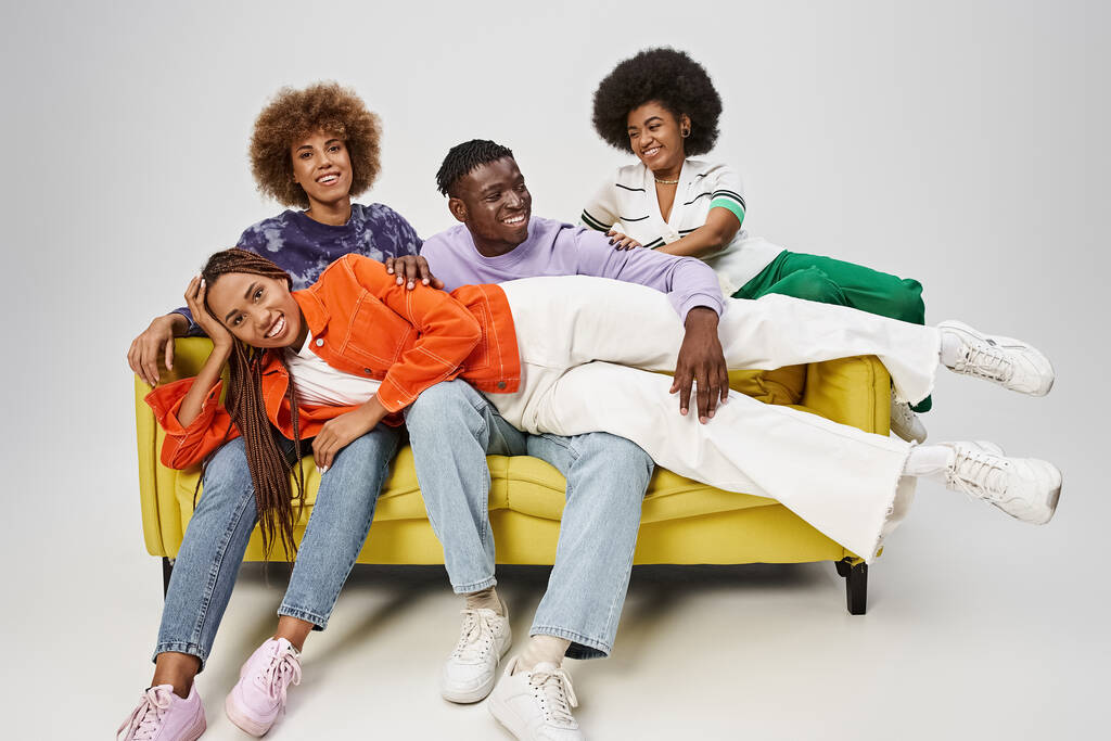 sonriente mujer afroamericana con rastas acostada en vueltas de amigos sentados en un sofá amarillo - Foto, imagen