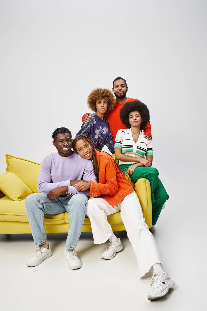 vidám afro-amerikai barátok színes alkalmi öltözékben együtt ülnek a sárga kanapén a szürkén. - Fotó, kép