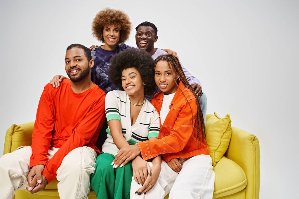 весёлая африканская американская община в красочной повседневной одежде, сидящая вместе на жёлтом диване на сером - Фото, изображение