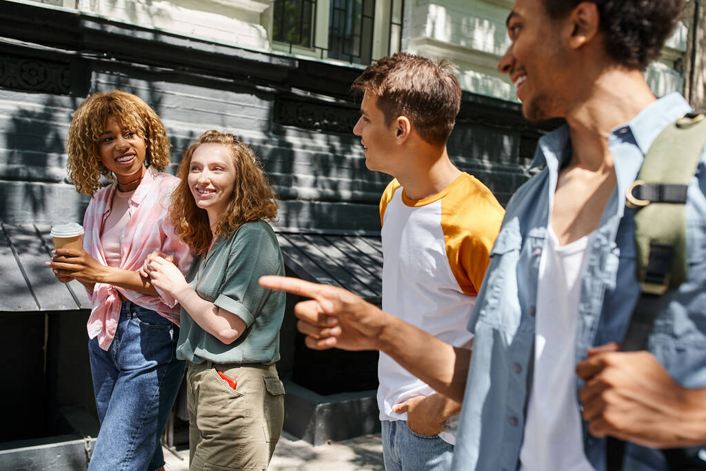 усміхнений афроамериканський чоловік вказує пальцем біля стильних багатоетнічних друзів на міській вулиці - Фото, зображення