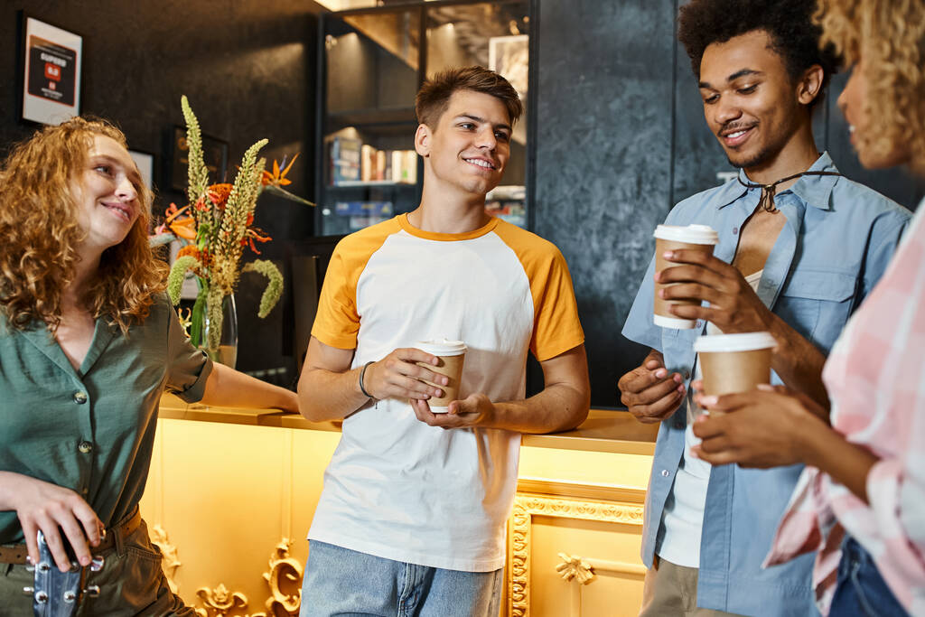 amigos multiétnicos alegres com bebidas takeaway conversando na recepção no albergue da juventude, viagens - Foto, Imagem